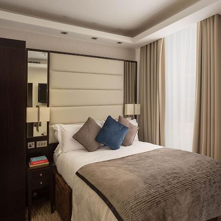 Montcalm Brewery Townhouse Hotel Londen Buitenkant foto The image shows a cozy bedroom. It features a comfortable double bed with a light-colored duvet and decorative pillows in shades of blue and gray. The headboard is upholstered in a soft material, and there are bedside lamps on either side of the bed.