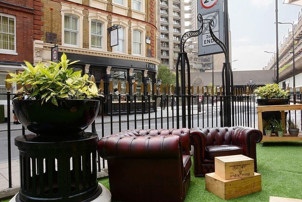 Montcalm Brewery Townhouse Hotel Londen Buitenkant foto The photo shows a street scene with a cozy outdoor seating area. There are two plush, dark leather couches arranged on green grass, creating a welcoming atmosphere. Surrounding the seating are large planters with vibrant plants. In the background, th