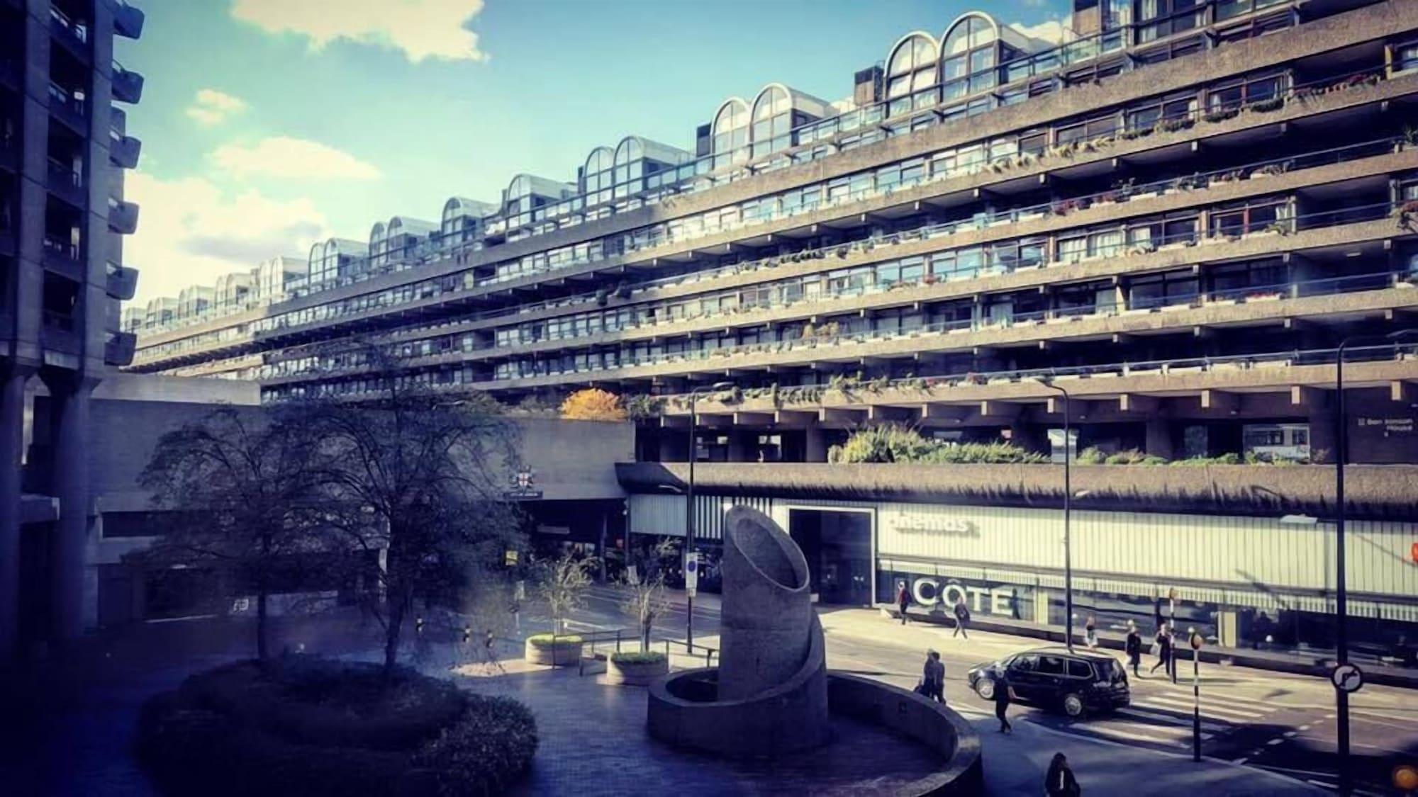 Montcalm Brewery Townhouse Hotel Londen Buitenkant foto The photo shows a modern architectural structure with multiple levels, featuring a series of large, rectangular balconies. Below this building, there is a plaza or courtyard area with a sculptural piece, which appears to be made of stone. Surrounding