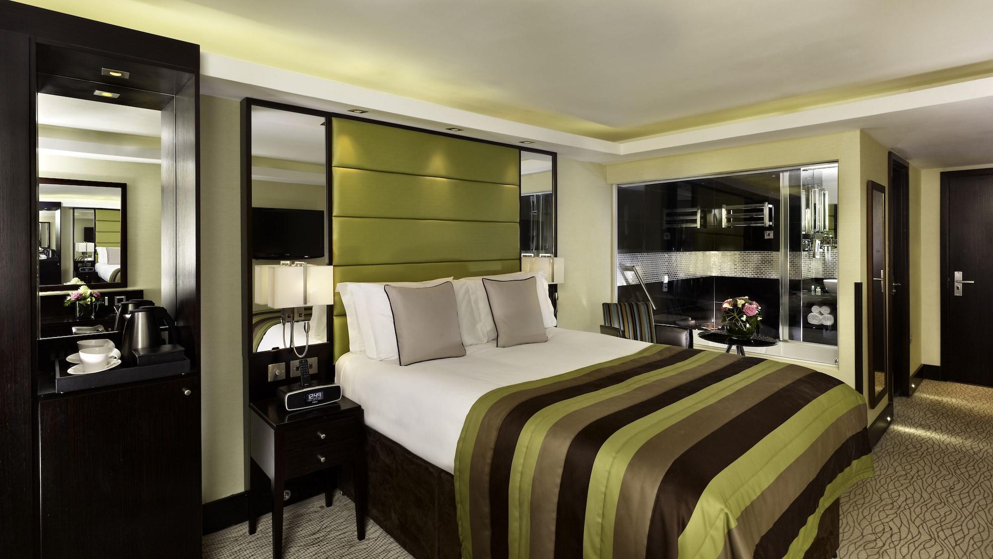 Montcalm Brewery Townhouse Hotel Londen Buitenkant foto The photo shows a modern hotel room designed with a sophisticated aesthetic. It features a comfortable double bed with a striped brown and green bedspread, complemented by two light gray decorative pillows. Behind the bed is an elegant headboard sect