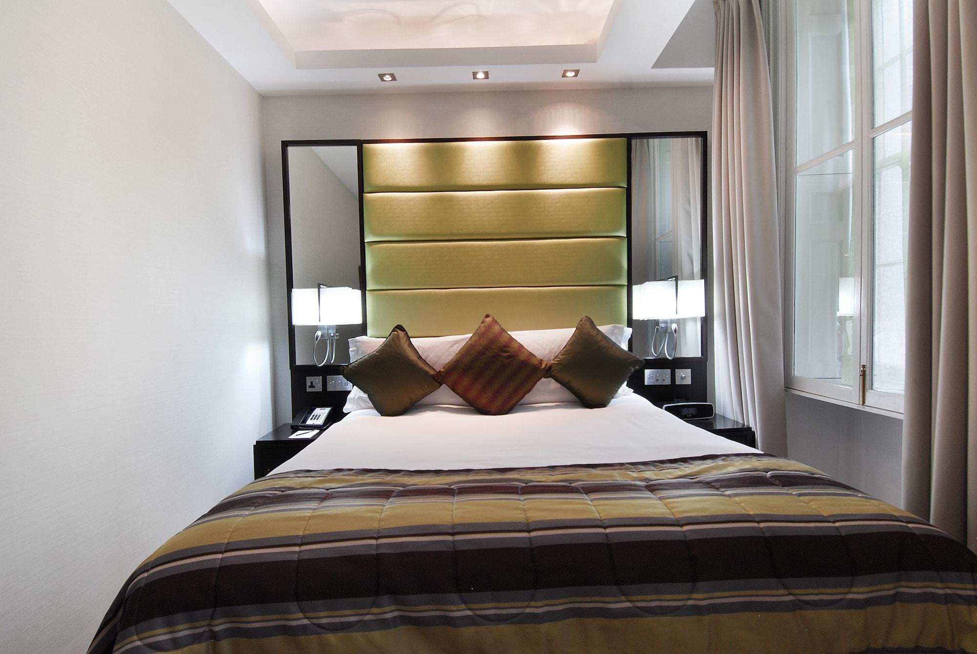 Montcalm Brewery Townhouse Hotel Londen Buitenkant foto The photo shows a stylishly decorated bedroom. The bed is centered in the room, featuring a white comforter with a plaid pattern in shades of brown and green. There are three decorative pillows on the bed, two in shades of brown and one in dark green