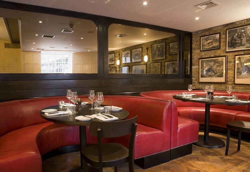 Montcalm Brewery Townhouse Hotel Londen Buitenkant foto The image shows the interior of a restaurant featuring a warm and inviting atmosphere. There are several round tables surrounded by black chairs, with red, upholstered booths lining the walls. The decor includes framed artwork hanging on the walls, a
