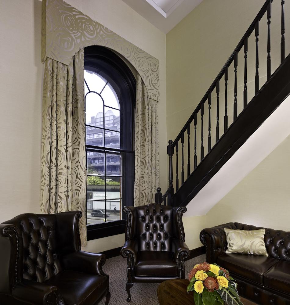 Montcalm Brewery Townhouse Hotel Londen Buitenkant foto The photo shows a cozy interior space featuring two elegant leather armchairs placed near a large, ornate window with arched top and decorative curtains. The wall is painted in a muted color, enhancing the warmth of the room. A staircase with black s