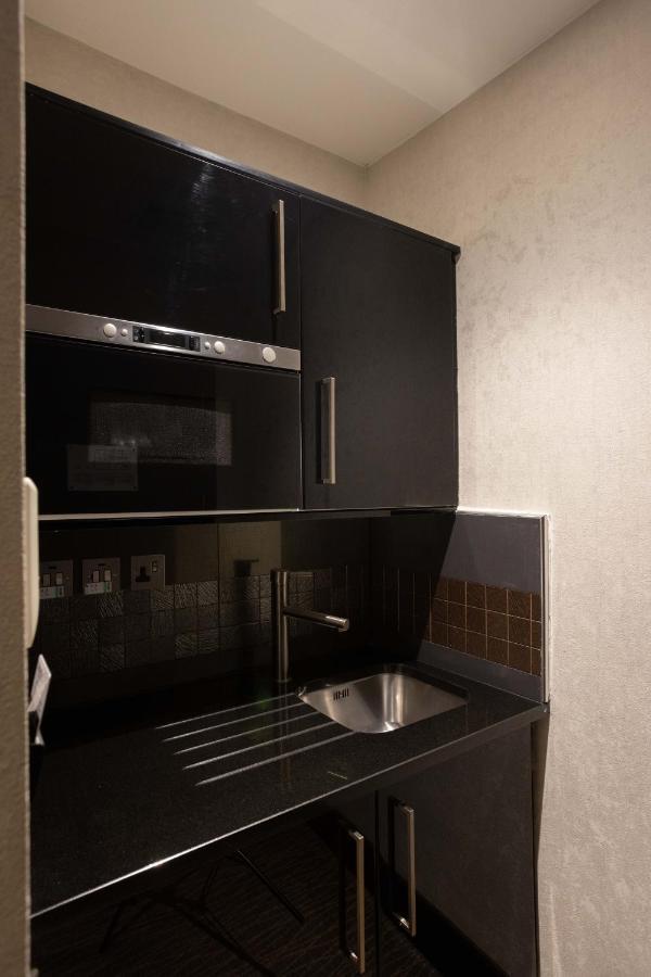 Montcalm Brewery Townhouse Hotel Londen Buitenkant foto The photo shows a modern kitchen setup with a dark color scheme. It features:

- A built-in microwave oven situated above a countertop.
- A sleek black cabinet beneath the microwave, which likely stores kitchen items.
- A stainless steel sink placed 
