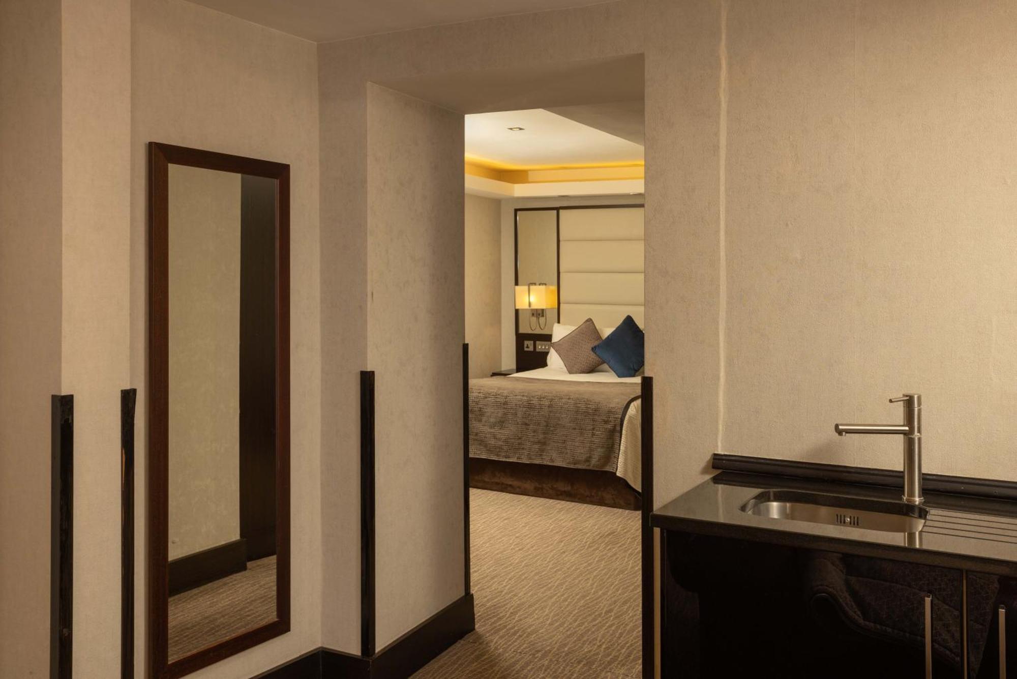 Montcalm Brewery Townhouse Hotel Londen Buitenkant foto The photo shows an interior space that appears to be part of a hotel room or suite. There is a doorway leading into a bedroom area, where a bed with decorative pillows is visible. In the foreground, there's a tall mirror on the left side and a small 