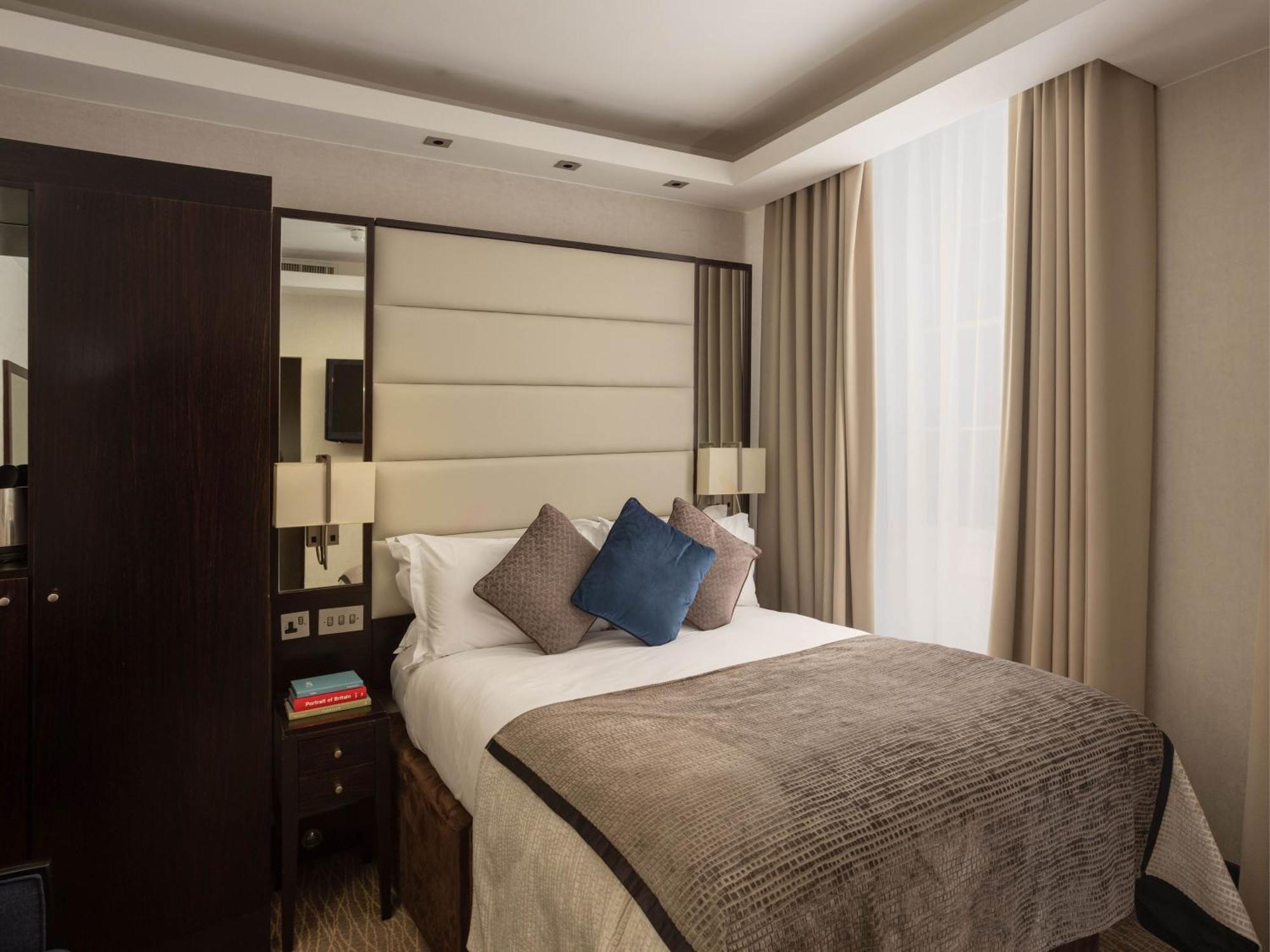 Montcalm Brewery Townhouse Hotel Londen Buitenkant foto The image shows a cozy bedroom. It features a comfortable double bed with a light-colored duvet and decorative pillows in shades of blue and gray. The headboard is upholstered in a soft material, and there are bedside lamps on either side of the bed.