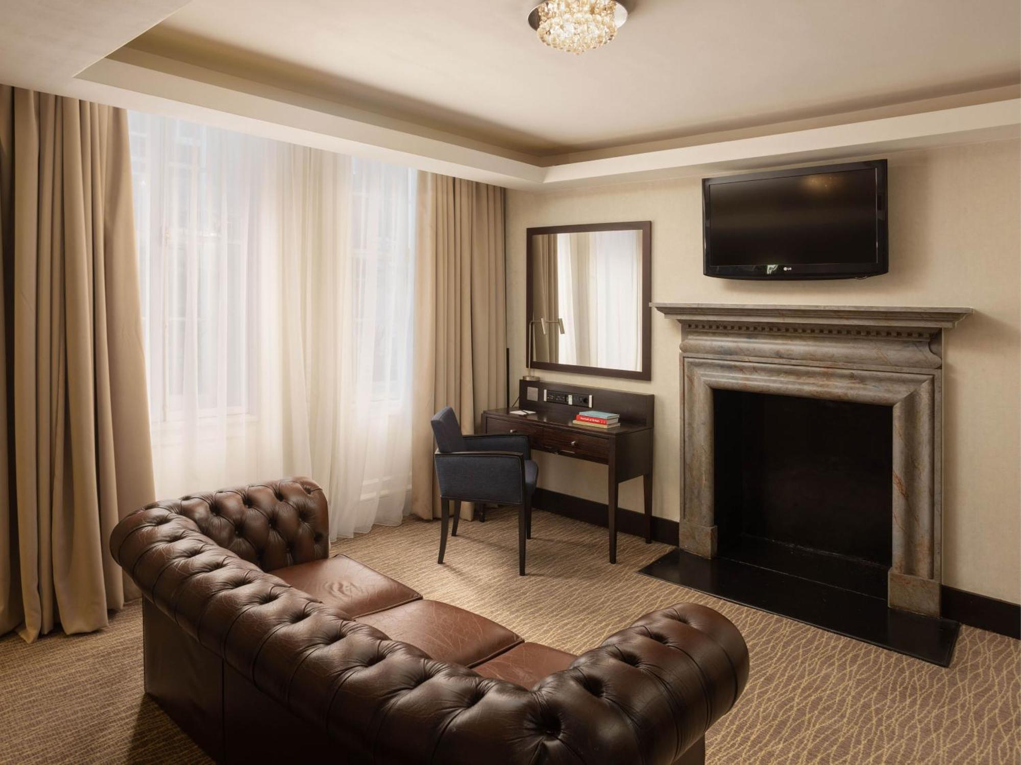 Montcalm Brewery Townhouse Hotel Londen Buitenkant foto The photo shows a cozy and elegantly designed room. There is a comfortable brown leather sofa with tufted detailing. A small desk and chair are positioned near a mirror, providing a space for work or personal grooming. On the wall, a flat-screen TV i