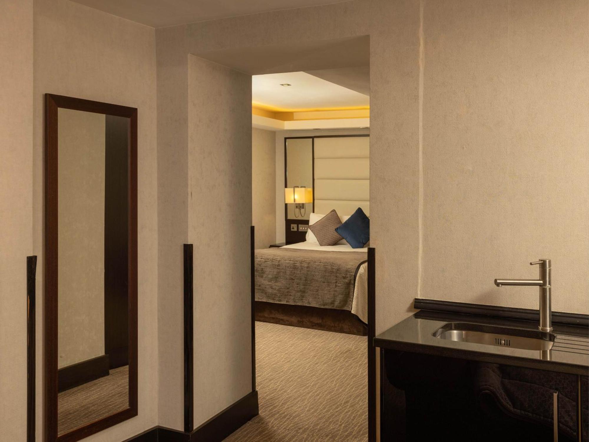 Montcalm Brewery Townhouse Hotel Londen Buitenkant foto The photo shows an interior space that appears to be a hotel room or a suite. There is a doorway leading to a bedroom visible in the background, where a bed with decorative pillows can be seen. To the side, there is a small wet bar or kitchenette are