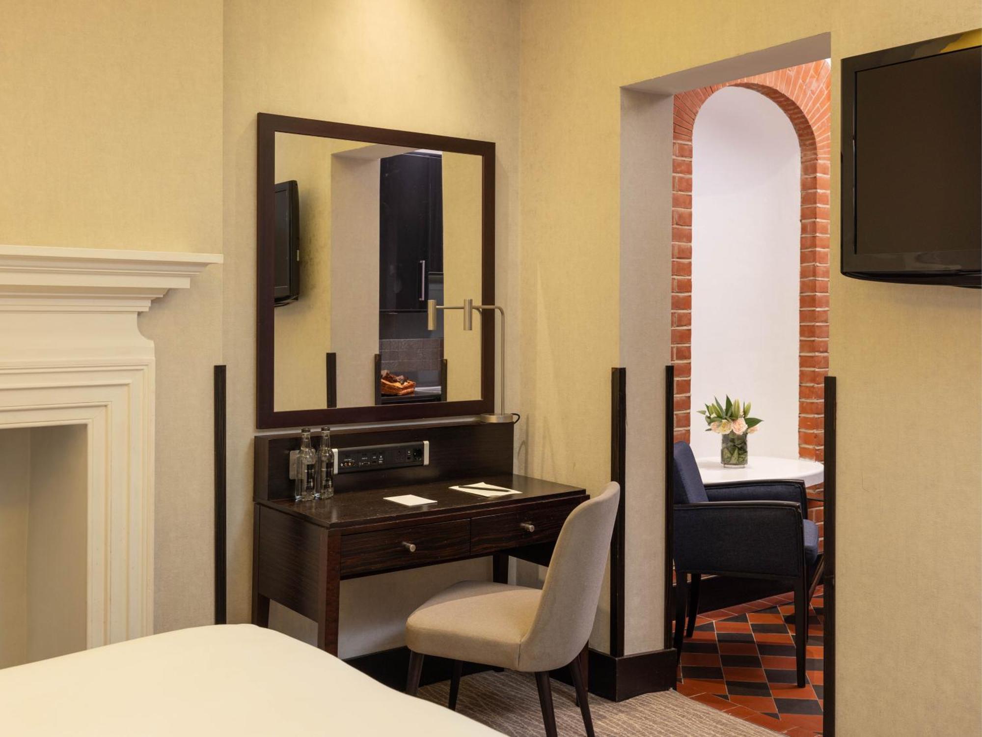 Montcalm Brewery Townhouse Hotel Londen Buitenkant foto The photo displays a hotel room setup. On the left side, there's a bed with a simple white bedding arrangement. Adjacent to the bed, there's a wooden desk with a chair, along with a mirror above the desk. The desk area is equipped with some glassware