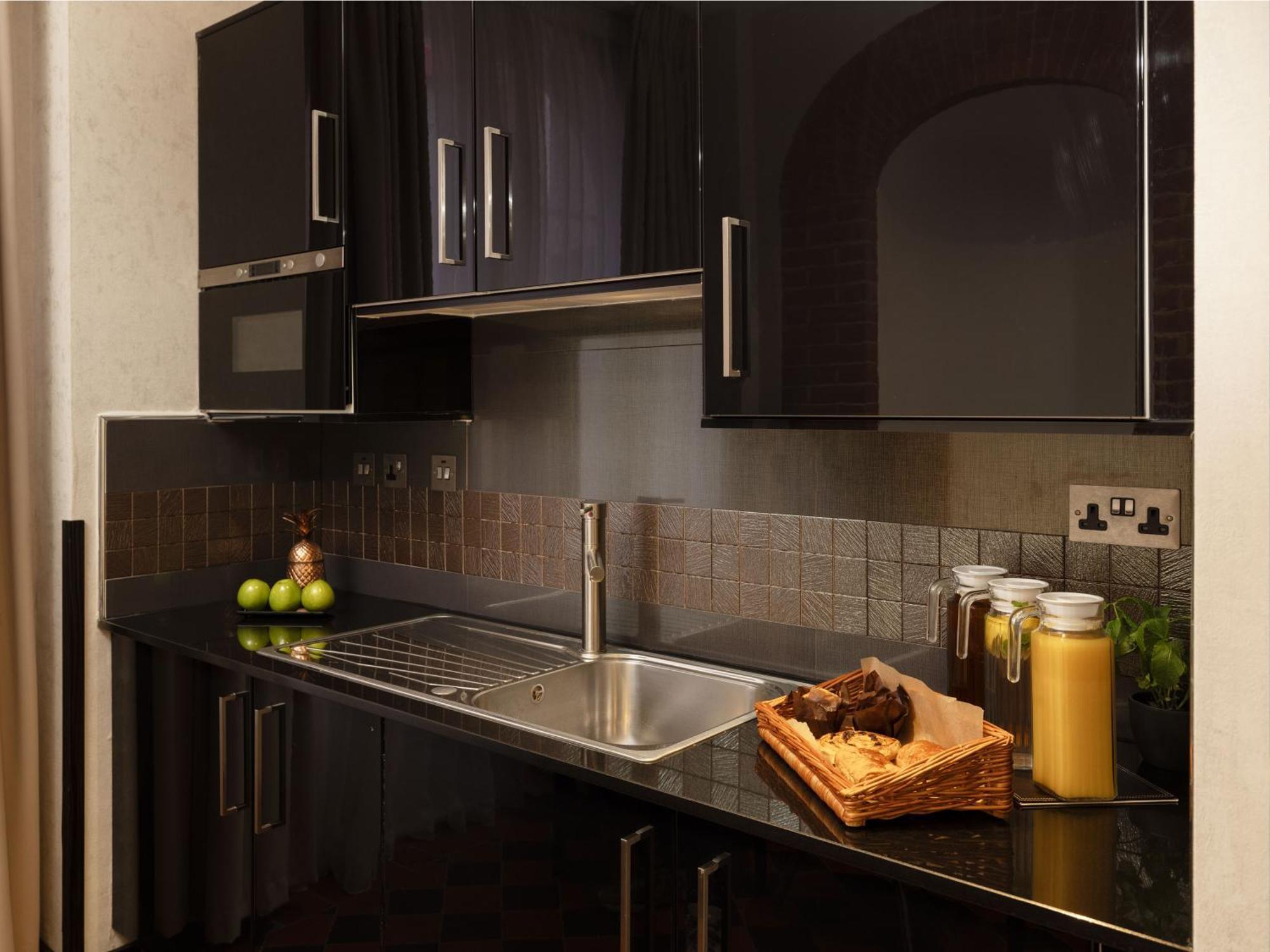 Montcalm Brewery Townhouse Hotel Londen Buitenkant foto The photo shows a modern kitchen with sleek black cabinetry and a glossy finish. The kitchen features a stainless steel sink with a contemporary faucet, set against a dark, textured countertop. Above the counter, there are cabinets that match the cou