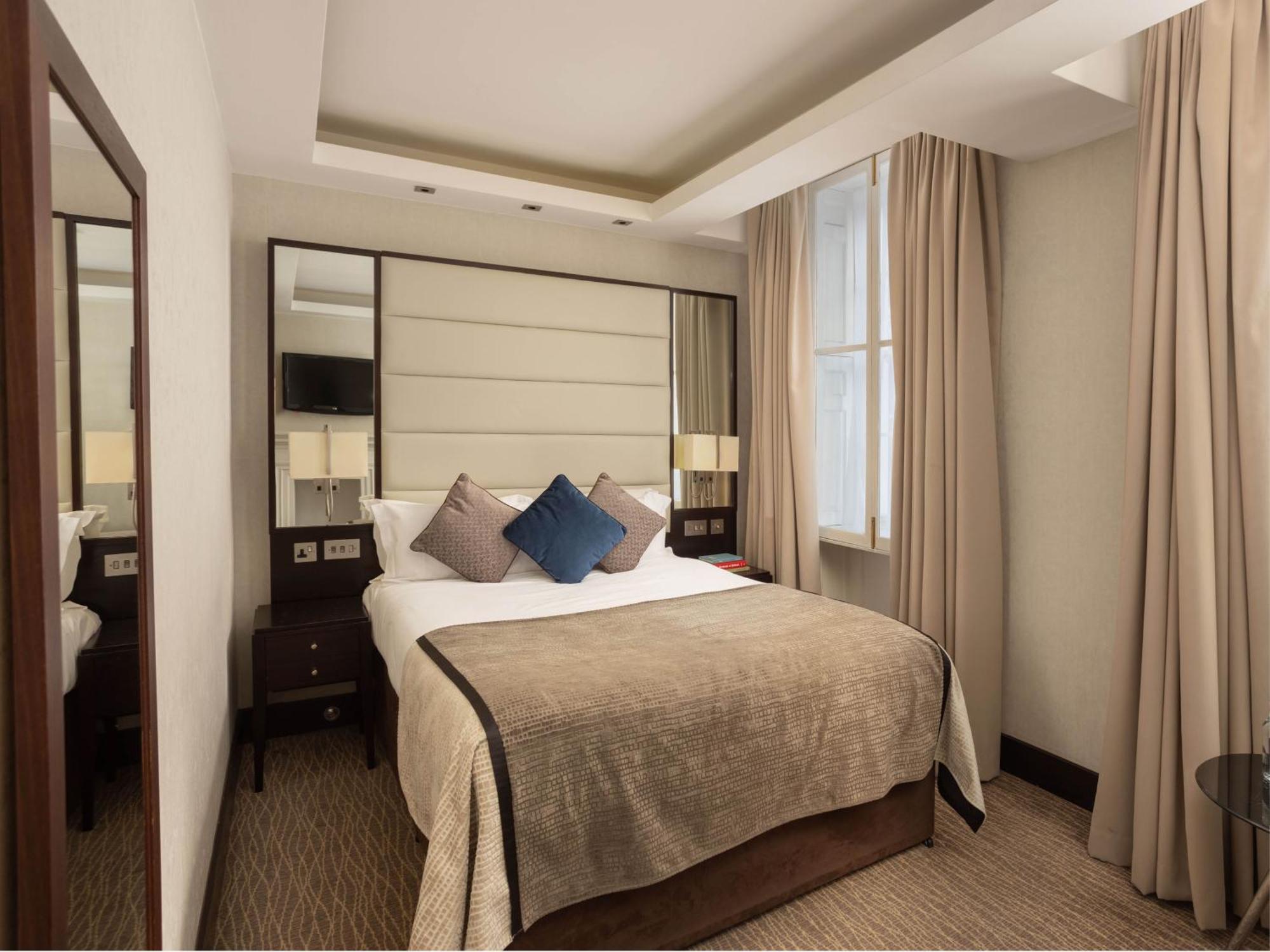 Montcalm Brewery Townhouse Hotel Londen Buitenkant foto The photo shows a cozy hotel room with a bed as the focal point. The bed is made with neutral-colored linens and has several pillows, including a decorative blue one. There are bedside tables on either side of the bed, each with a lamp. A large mirro
