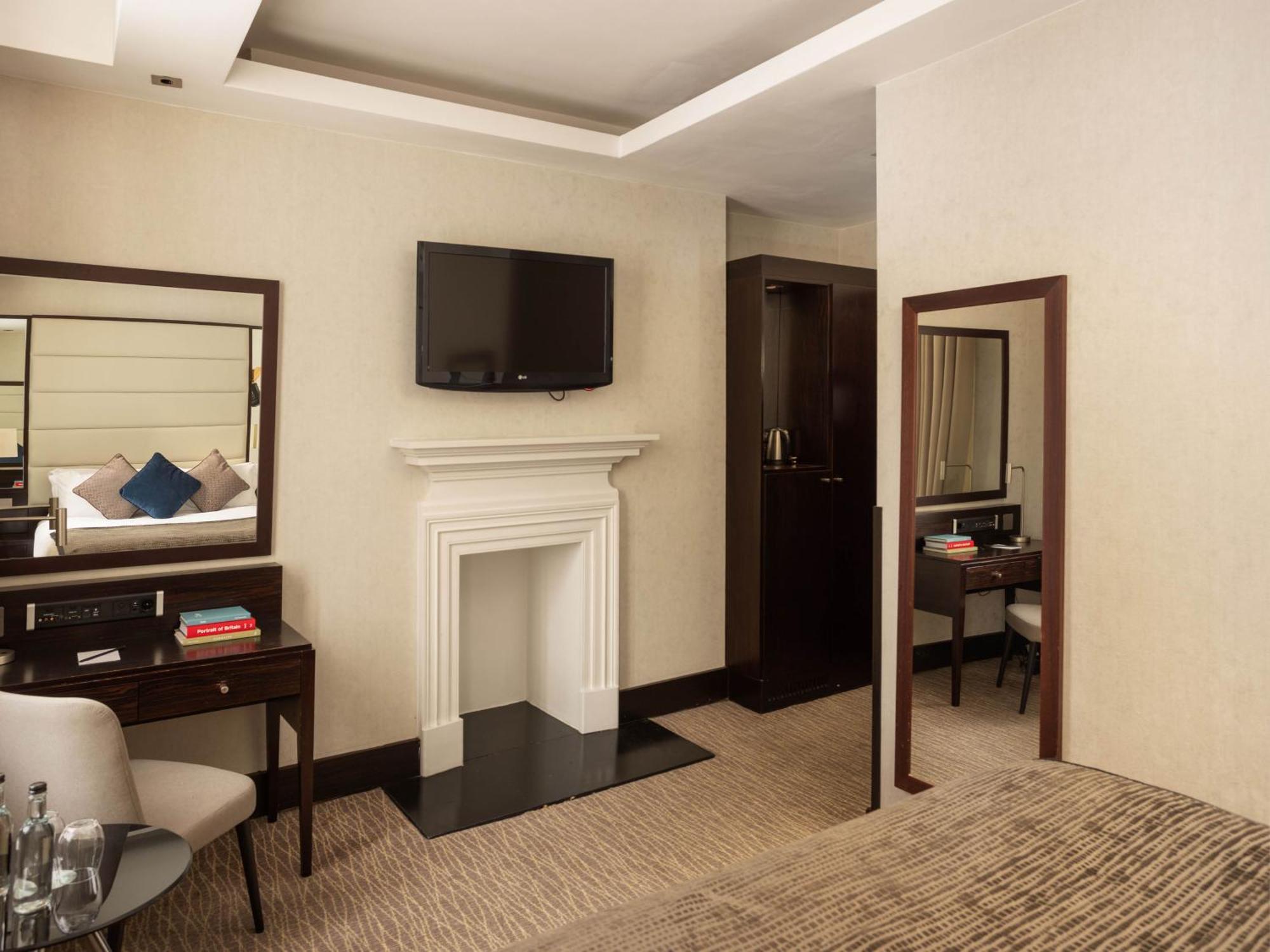 Montcalm Brewery Townhouse Hotel Londen Buitenkant foto The photo depicts a stylish hotel room. It features a double bed, a large flat-screen TV mounted on the wall, and a decorative fireplace. There is a wooden desk with a chair beside it, as well as a mirror hanging on the wall. The decor is modern and 