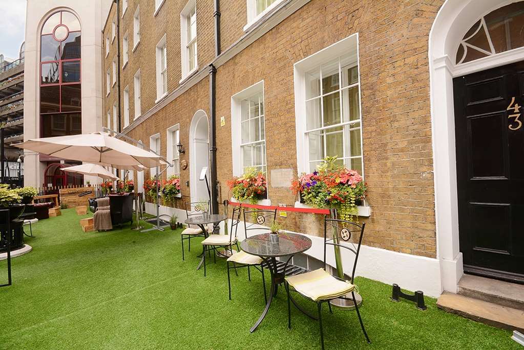 Montcalm Brewery Townhouse Hotel Londen Buitenkant foto The photo depicts a charming outdoor area in front of a building with a warm, textured brick facade. There is a neatly maintained lawn, likely made of artificial grass, and several small round tables with chairs are arranged outside. Flower pots with