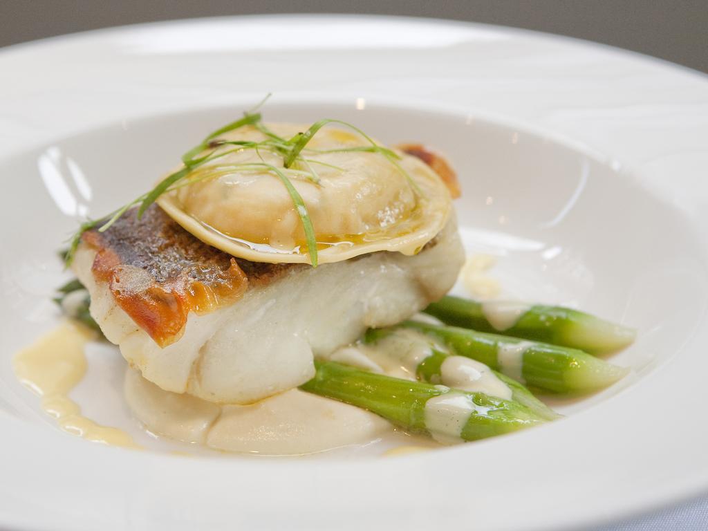 Montcalm Brewery Townhouse Hotel Londen Buitenkant foto The image shows a beautifully presented dish featuring a piece of fish, likely a white fish, topped with a clam. It is served on a bed of green asparagus spears. The dish is garnished with thinly sliced herbs or greens, adding a touch of color. The s