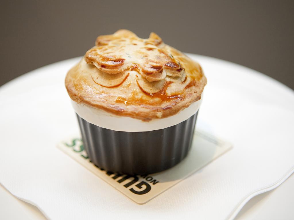 Montcalm Brewery Townhouse Hotel Londen Buitenkant foto The photo shows a small, individual serving of a pie, likely a savory dish. It has a golden-brown crust with decorative elements on top, resembling leaves or floral patterns. The pie is served in a black dish and placed on a white plate. The overall 