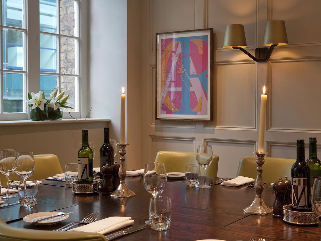 Montcalm Brewery Townhouse Hotel Londen Buitenkant foto The photo shows an elegantly set dining room with a large wooden table surrounded by several chairs. The table is adorned with neatly arranged utensils, glasses, and decorative items. There are two tall candlesticks with candles and several bottles o