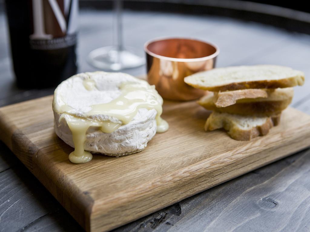Montcalm Brewery Townhouse Hotel Londen Buitenkant foto The photo features a wooden serving board with several items. There is a round cheese, likely Brie or a similar soft cheese, that appears to be melting and dripping slightly. Next to the cheese, there is a small copper cup that might contain a sauce 