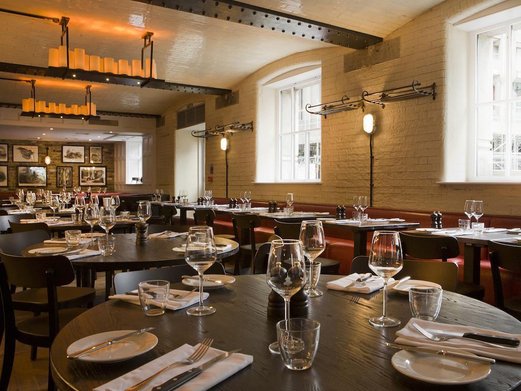 Montcalm Brewery Townhouse Hotel Londen Buitenkant foto The photo shows a restaurant interior featuring a warm and inviting atmosphere. It has several round wooden tables set for dining, each with neatly arranged plates, utensils, and glasses. The lighting is soft, with overhead fixtures providing a cozy 
