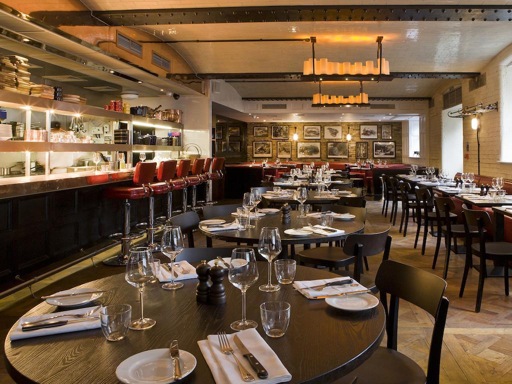 Montcalm Brewery Townhouse Hotel Londen Buitenkant foto The photo shows the interior of a stylish restaurant. It features several round tables set with white plates, glasses, and silverware, all neatly arranged for dining. The decor includes a modern design with wooden floors and a mix of lighting fixture