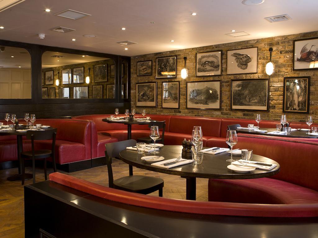 Montcalm Brewery Townhouse Hotel Londen Buitenkant foto The photo depicts an elegant restaurant interior. There are curved red booths along the walls, creating a cozy seating arrangement. The tables are round and set with white plates and glassware, indicating a prepared dining area. The walls feature a n
