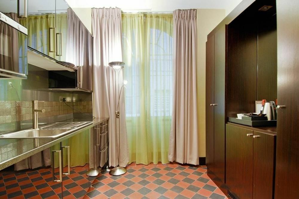 Montcalm Brewery Townhouse Hotel Londen Buitenkant foto The photo shows a modern kitchen area. There is metallic cabinetry and a stainless steel countertop with a sink. The walls are adorned with light-colored curtains that allow natural light to filter in, with one set in a soft purple hue and another in
