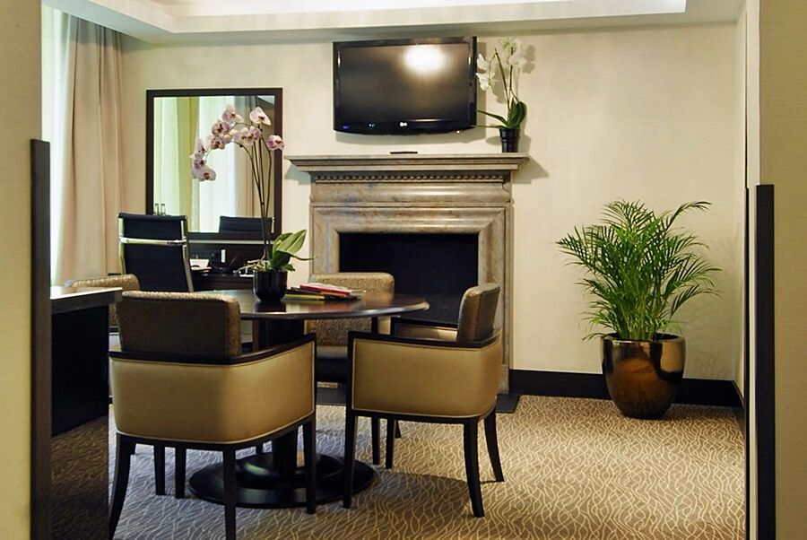 Montcalm Brewery Townhouse Hotel Londen Buitenkant foto The photo shows a modern and stylish room with a dining or meeting area. There is a round table surrounded by four upholstered chairs. A flat-screen television is mounted on the wall above a decorative fireplace. To the side, there is a mirror reflec